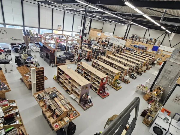 Overzicht van kringloopwinkel met houten stellingen vol boeken, huishoudartikelen en diverse tweedehandsartikelen