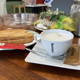 Kopje koffie met Backstad-logo, koekjes en brood op houten tafel in lunchroom