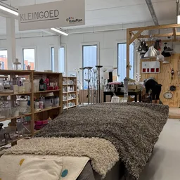 Winkelinterieur met houten stellingen, tafels met grijze en beige tapijten, diverse spullen en artikelen
