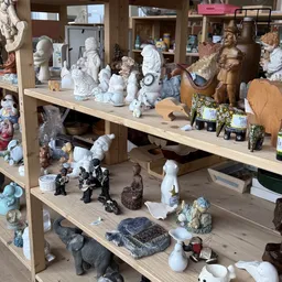 Houten stellingen met diverse beeldjes, sculpturen en decoratieve objecten in verschillende materialen en kleuren