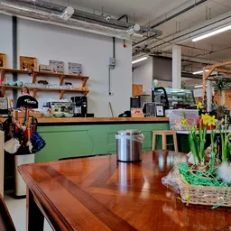 Winkelinterieur met houten tafel, groene balie, houten stellingen en bloemstuk op voorgrond