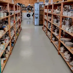 Winkelgang met houten stellingen vol servies, kopjes en huishoudelijke spullen aan beide zijden