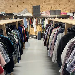 Overzicht van kringloopwinkel met kledingrekken vol tweedehands kleding en houten stellingen tegen de muur