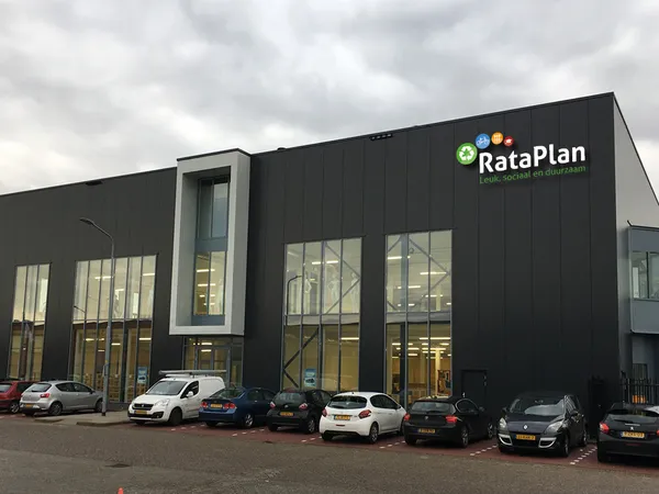 Moderne zwarte gevel van RataPlan kringloopwinkel met grote ramen en parkeerplaats met auto's