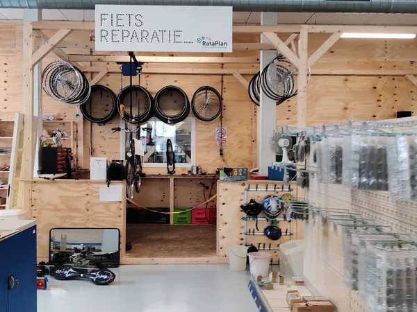Fietswerkplaats met gereedschappen en onderdelen opgehangen aan houten wand, fiets in het midden, groene en rode bakken voor 