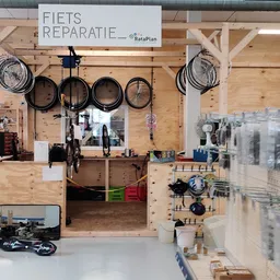 Fietswerkplaats met gereedschappen en onderdelen opgehangen aan houten wand, fiets in het midden, groene en rode bakken voor 