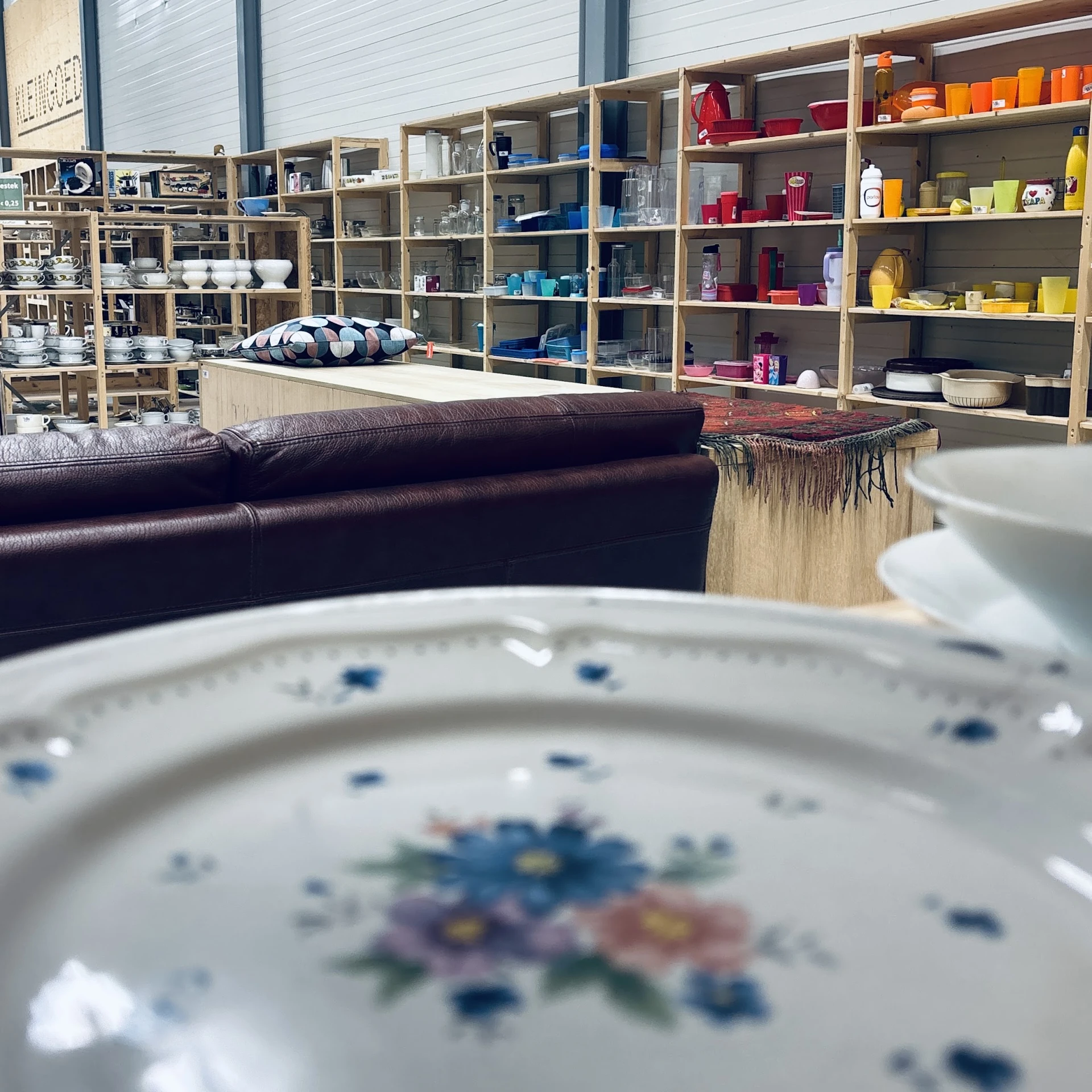 Close-up van een wit porseleinen bord met blauwe bloemmotief, op de achtergrond stellingen met servies en huishoudartikelen