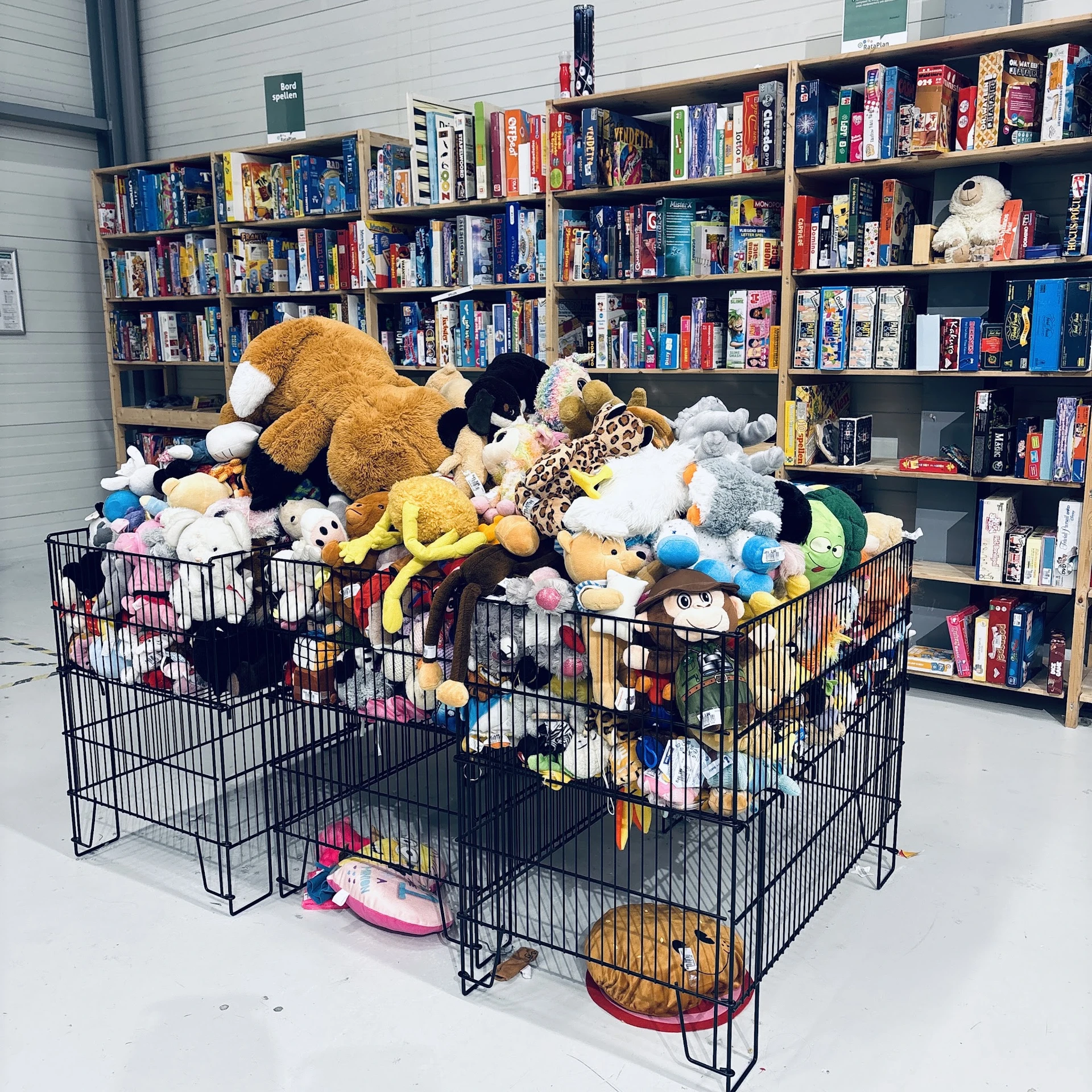 Grote zwarte box vol met knuffels en speelgoed, tegen achtergrond met boekenkasten