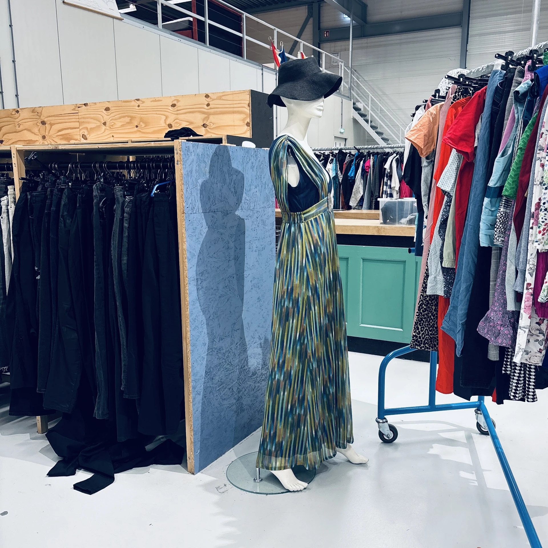 Rekken met tweedehands kleding, waaronder zwarte jurken en gekleurde kledingstukken, met mannequins in de kringloopwinkel.