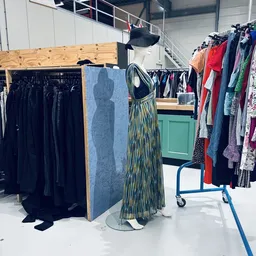 Rekken met tweedehands kleding, waaronder zwarte jurken en gekleurde kledingstukken, met mannequins in de kringloopwinkel.