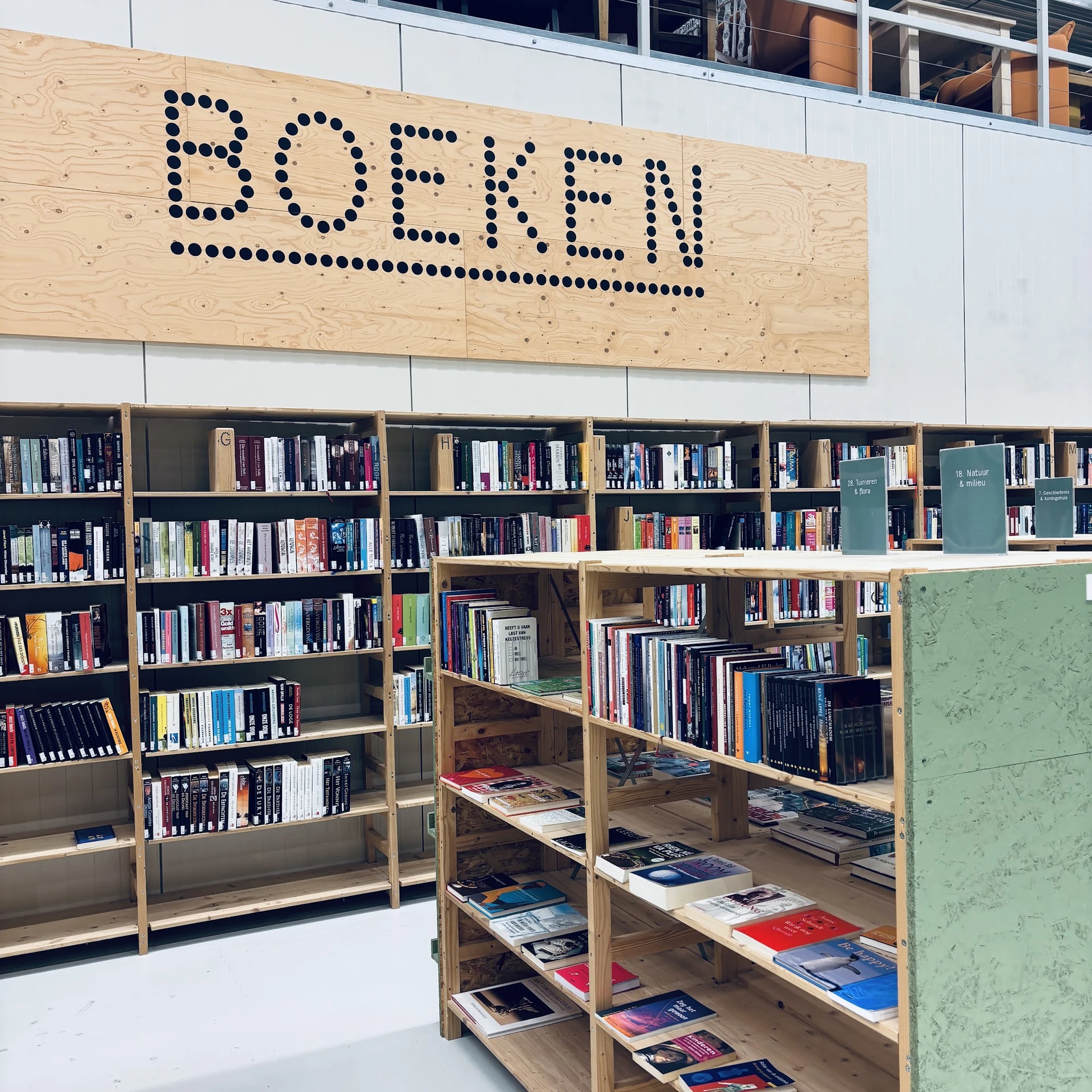 Boekenrekken in een kringloopwinkel met het woord 'BOEFEN' op een houten bord aan het plafond