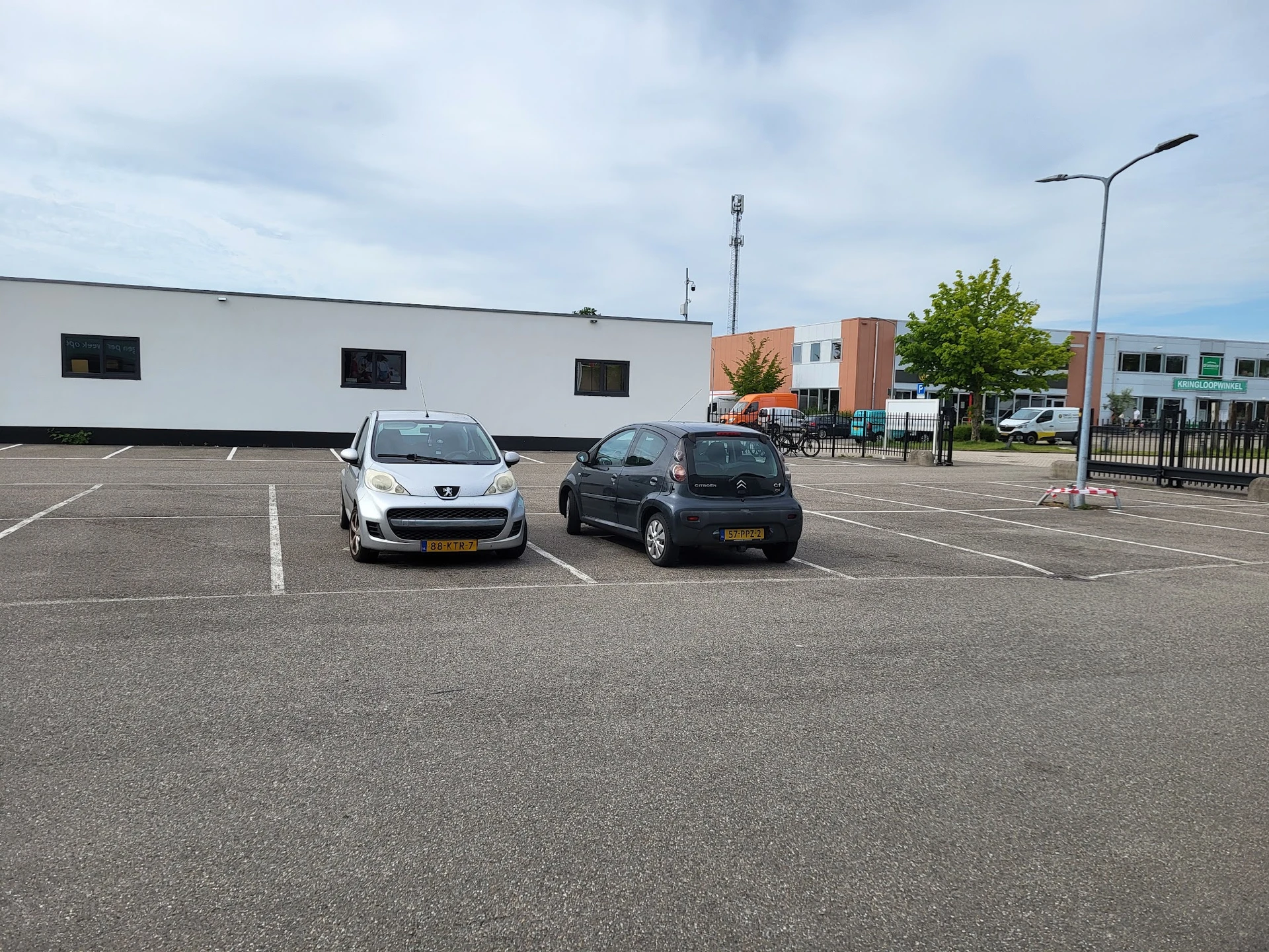 Parkeerplaats met twee auto's voor wit gebouw met ramen