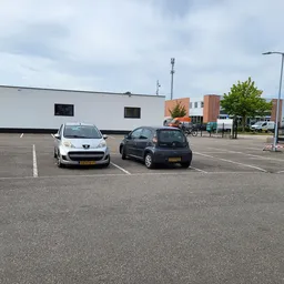 Parkeerplaats met twee auto's voor wit gebouw met ramen