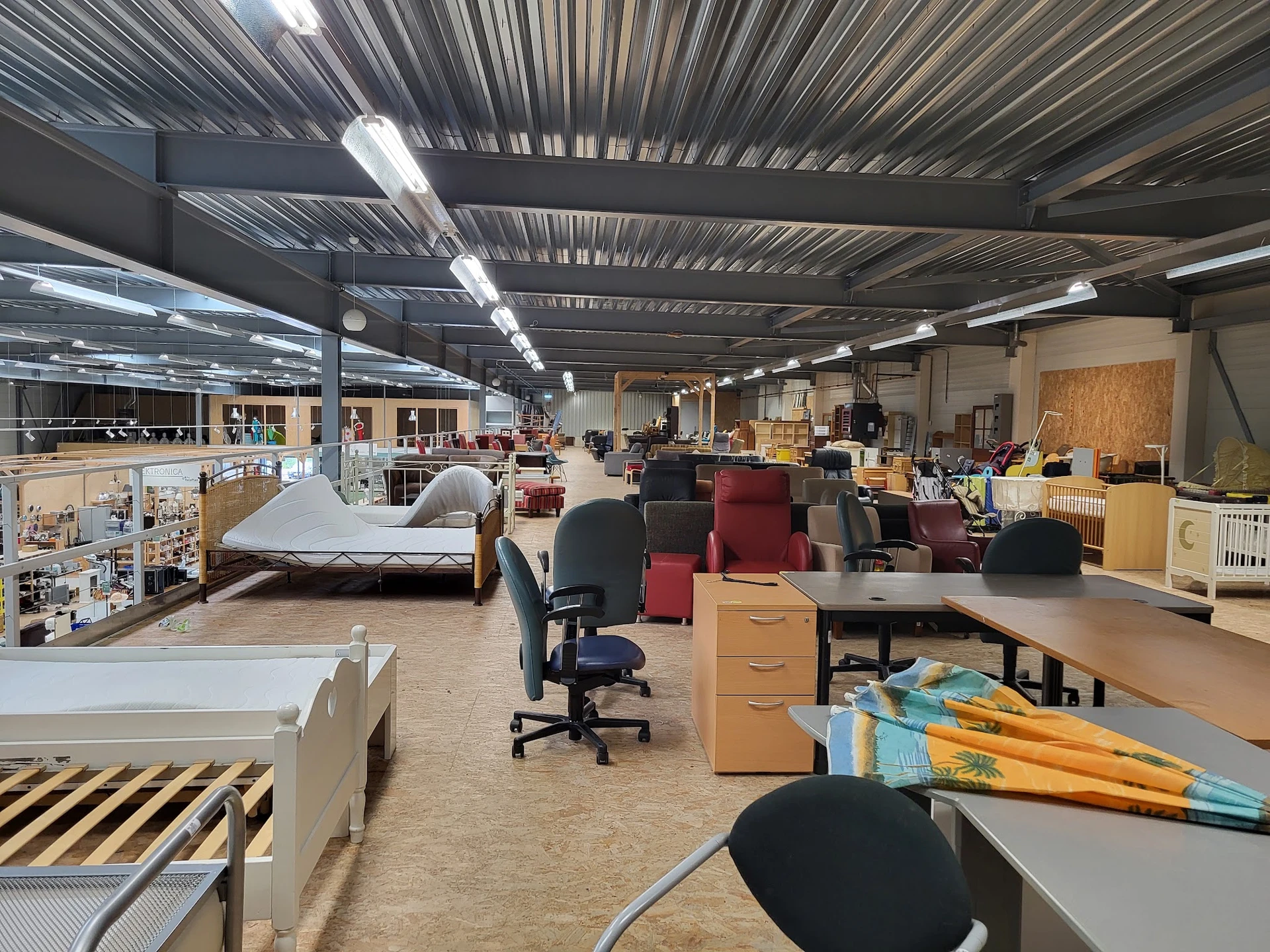 Ruime winkelhal met diverse tweedehands meubels, stoelen en huisraad uitgestald op de vloer en tegen de wanden