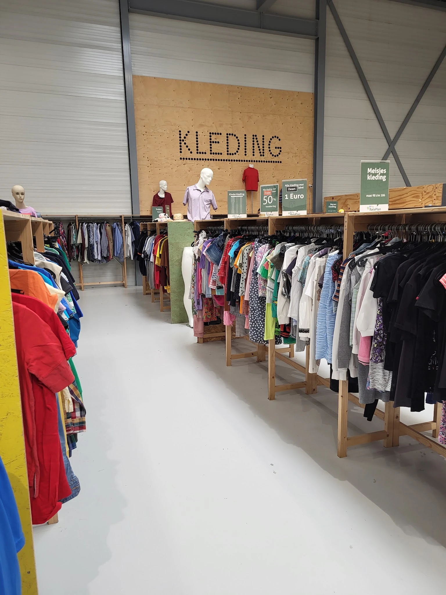 Winkelvloer met houten kledingrekken vol tweedehands kleding, uitstallingen en bord met 'KLEDING' boven