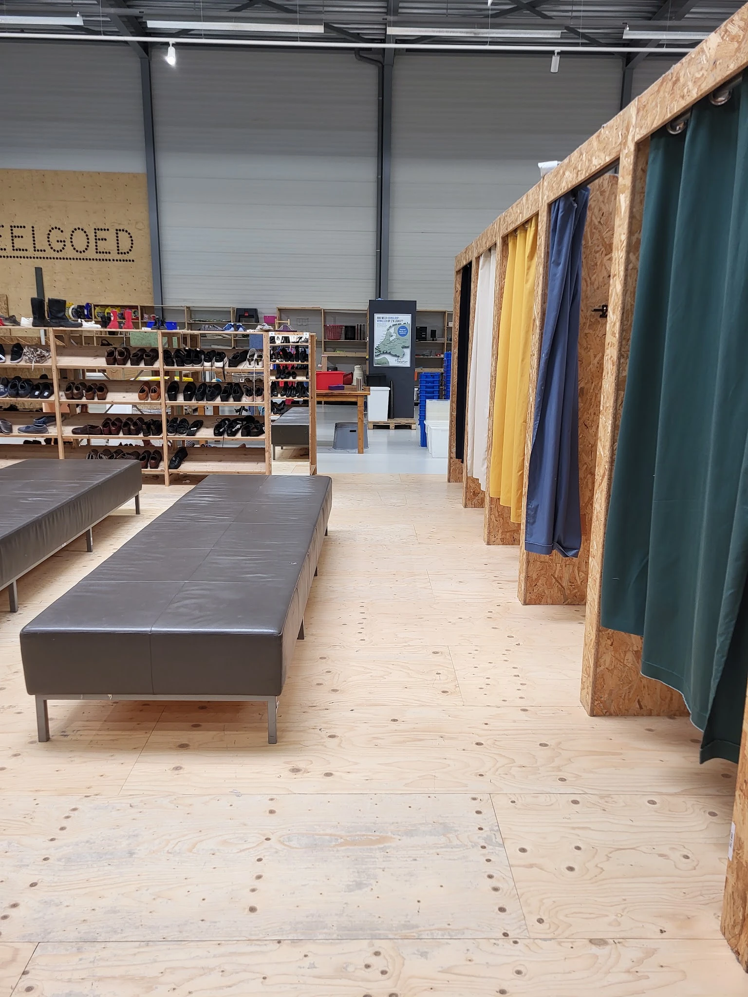 Winkelruimte met lange grijze bank, schoenrekken, kleding aan rails en houten vloer