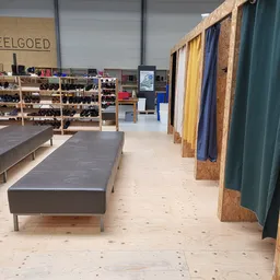 Winkelruimte met lange grijze bank, schoenrekken, kleding aan rails en houten vloer