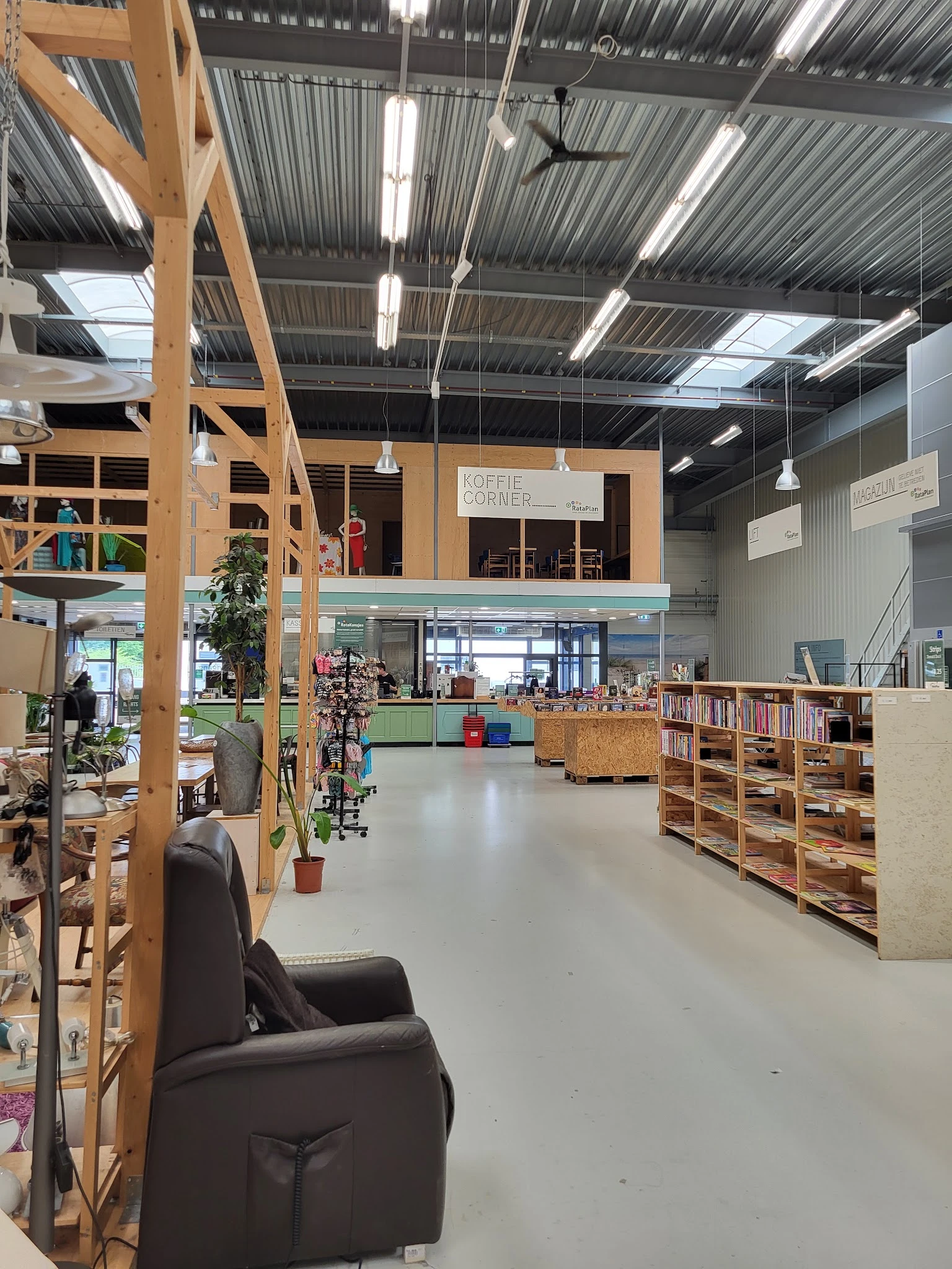 Ruim interieur van kringloopwinkel met houten stellingen, boeken, boekenkasten en een koffiehoek