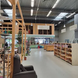 Ruim interieur van kringloopwinkel met houten stellingen, boeken, boekenkasten en een koffiehoek