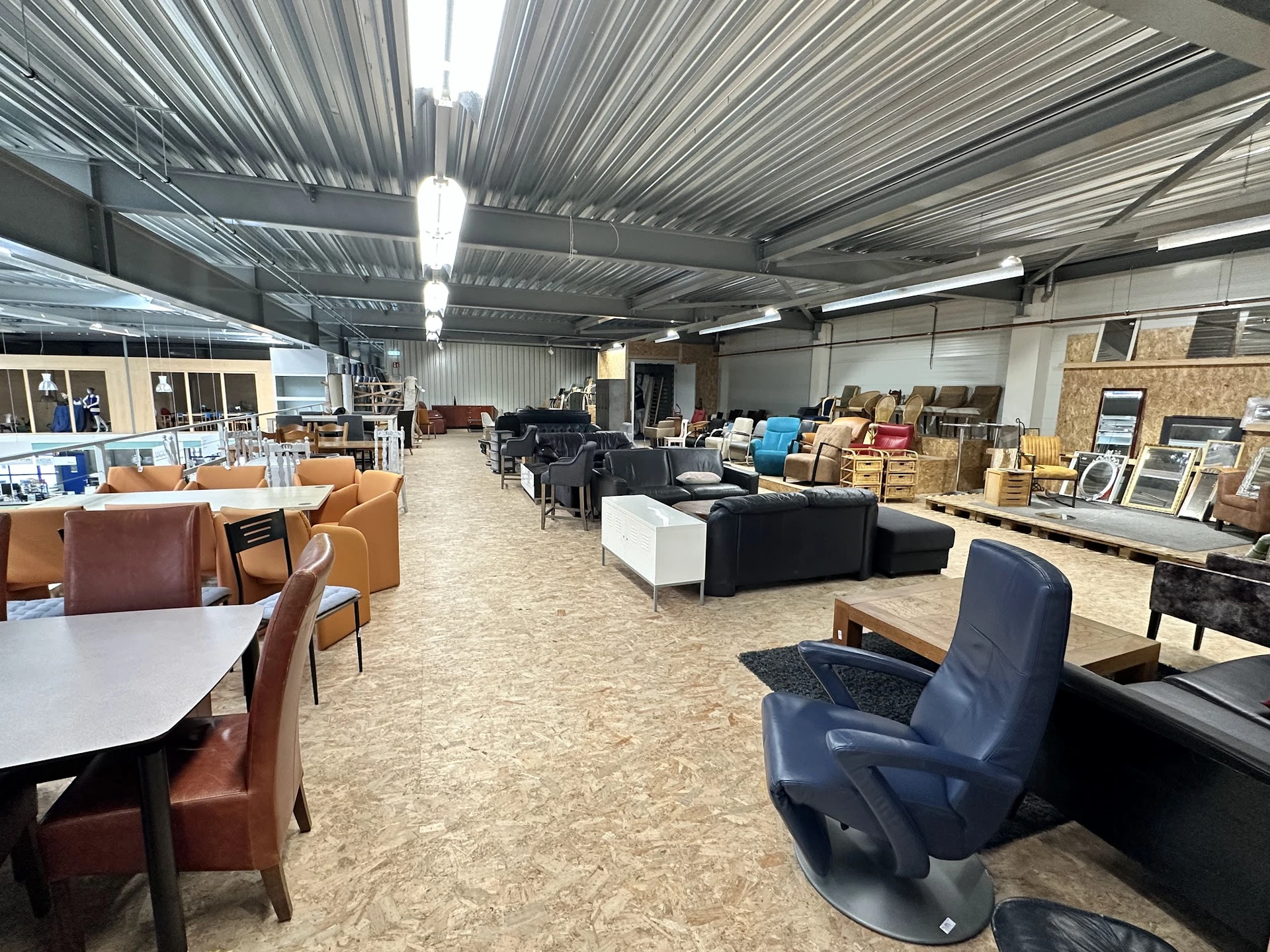 Ruime winkelvloer met diverse meubelen, stoelen en huishoudartikelen uitgestald onder industrieel plafond met daglicht