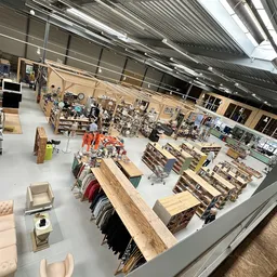 Overzicht van de winkelvloer met diverse rekken, meubels en uitgestalde artikelen onder industriële verlichting