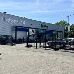Voorgevel van kringloopwinkel RataPlan met grijze golfplaten, grote ramen, zwarte hekken en parkeerplaats