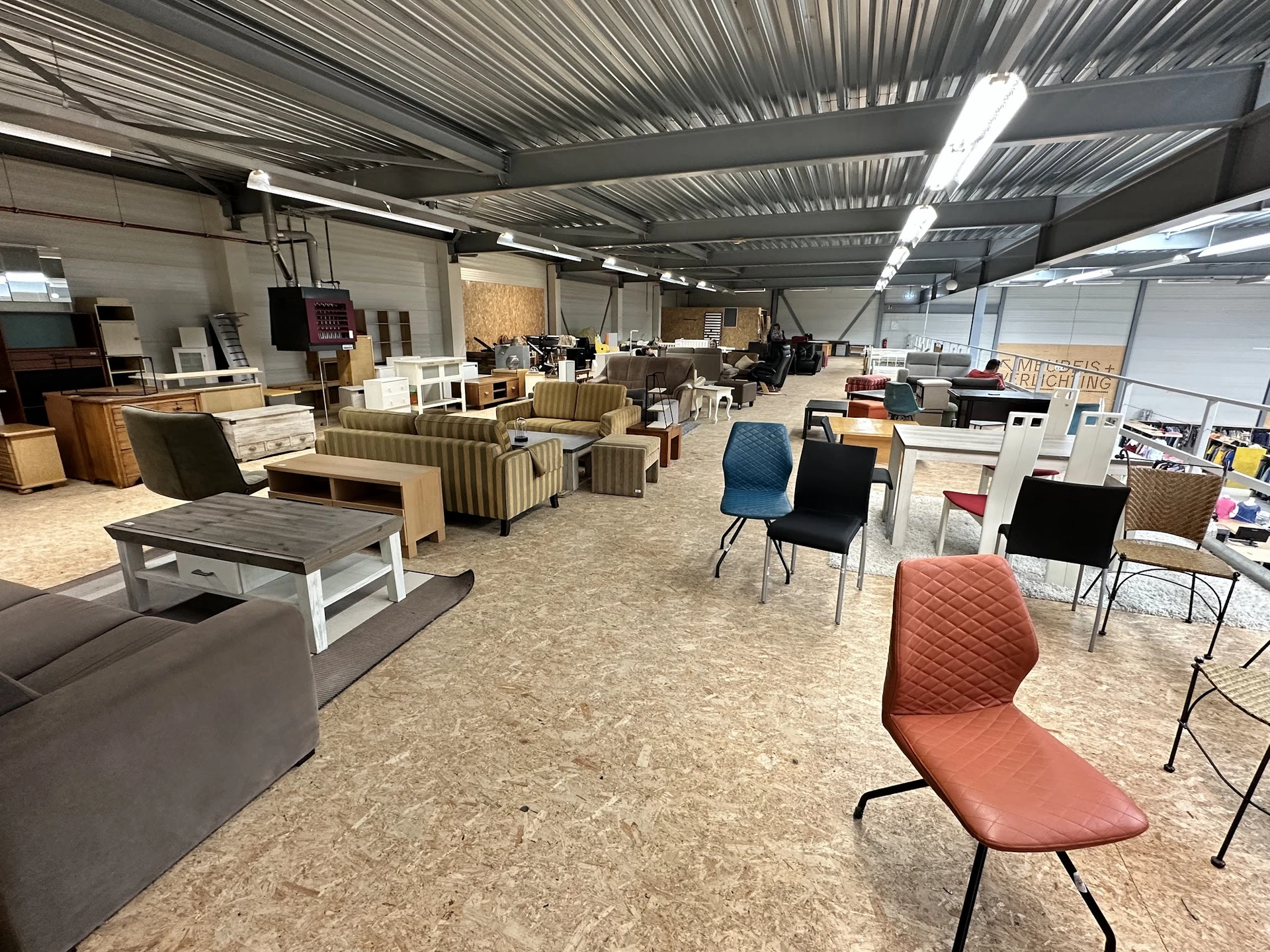 Winkelvloer met diverse meubels en stoelen uitgestald in een grote hal met golfplaten dak