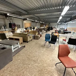 Winkelvloer met diverse meubels en stoelen uitgestald in een grote hal met golfplaten dak