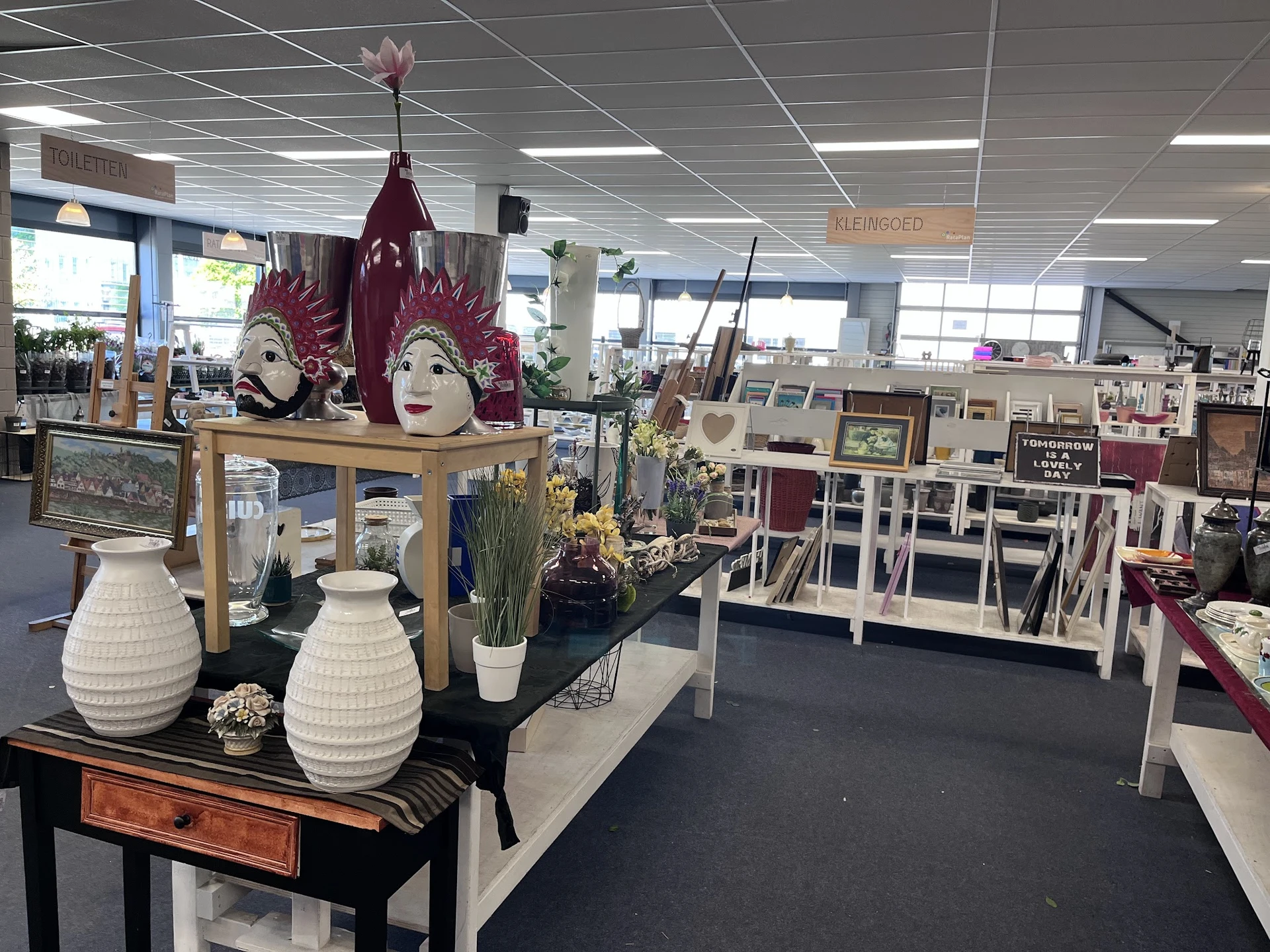 Winkelvloer met diverse decoratieve artikelen, stellingen en uitgestalde koopwaar in een ruime ruimte met plafondverlichting