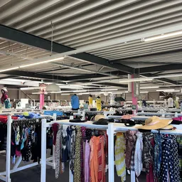 Ruim winkelinterieur met witte stellingen vol tweedehands kleding en felgekleurde palen, industrieel plafond met LED-verlicht