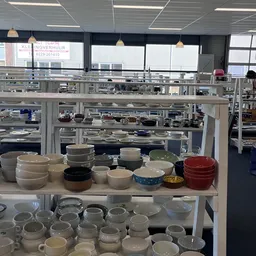 Uitgestalde serviesgoed en huishoudelijke artikelen op planken in de kringloopwinkel