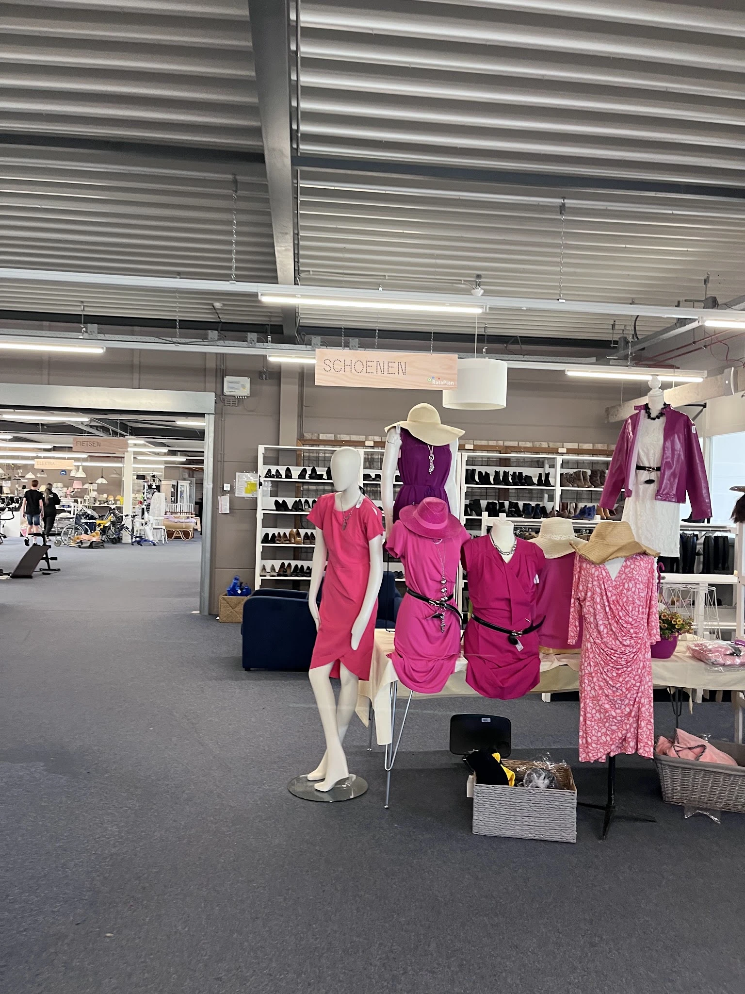 Uitgestalde dameskleding in roze en paarse tinten op mannequins en kledingrekken in de winkel