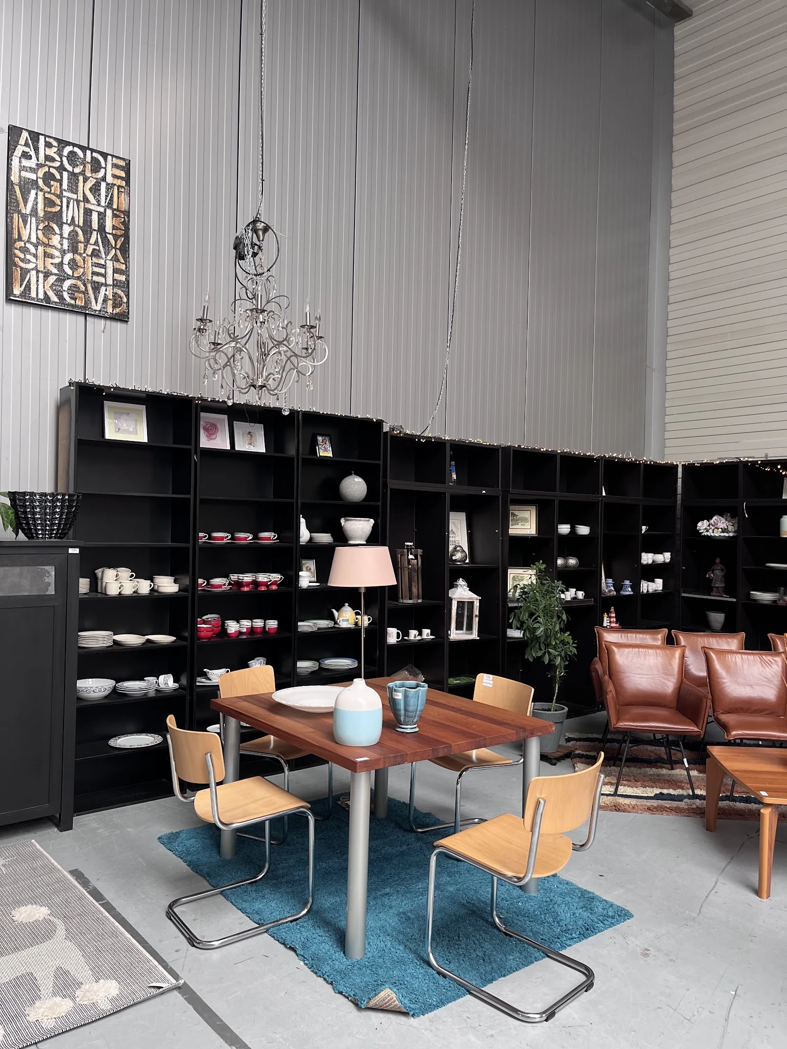 Winkelinterieur met zwarte open stellingkasten vol servies en decoratieve items, houten tafel met stoelen en leren bank op de