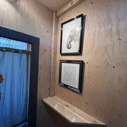 Hoek van een winkelruimte met houten wanden, twee ingelijste afbeeldingen waarvan één olifant, en een deuropening met blauw g