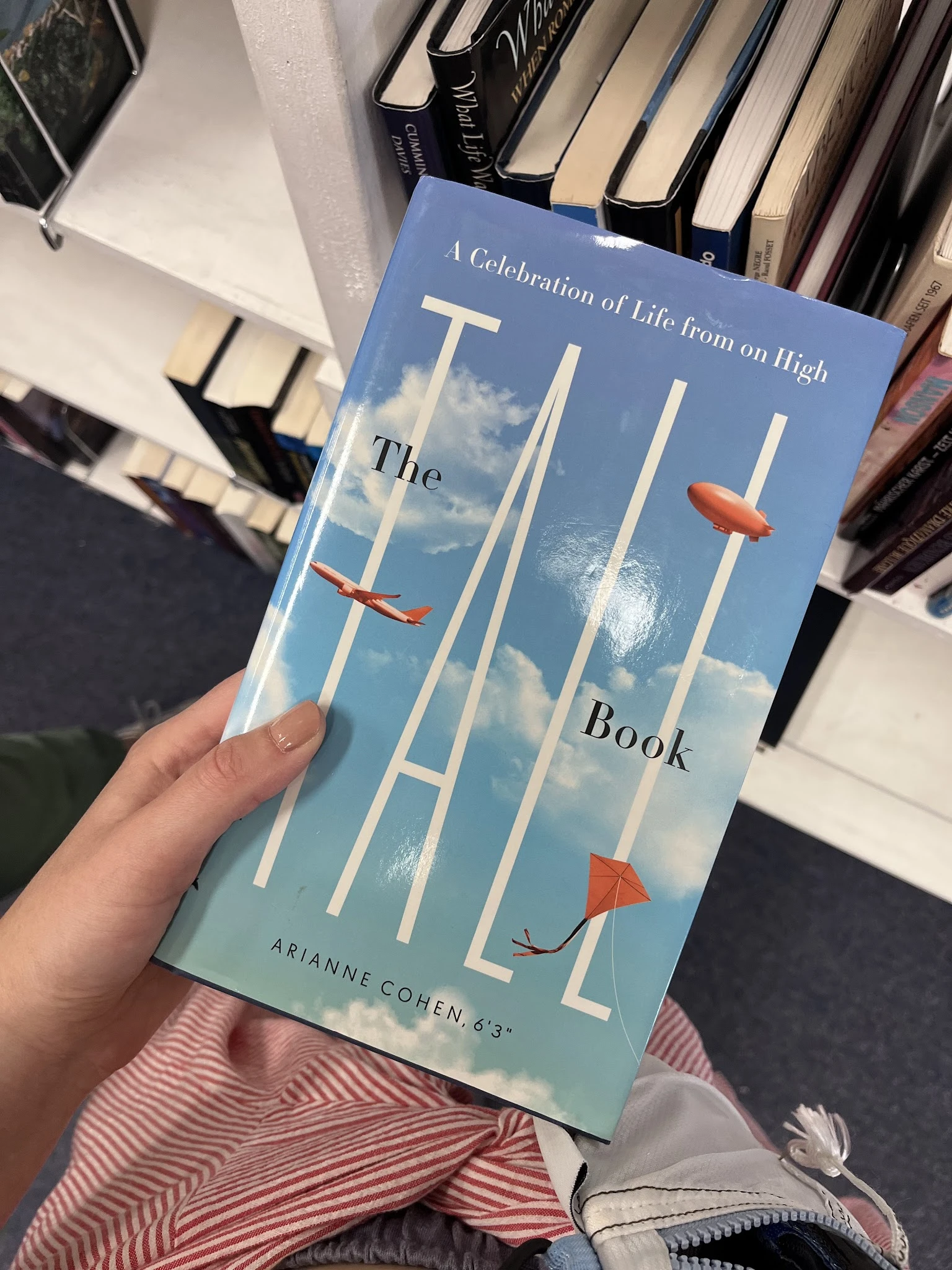 Close-up van het boek 'The Tall Book' met blauwe omslag en rode vliegers, gehouden in een hand