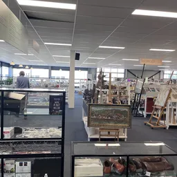 Winkelvloer van kringloopwinkel met schilderijen, houten rekken, meubels en diverse spullen uitgestald