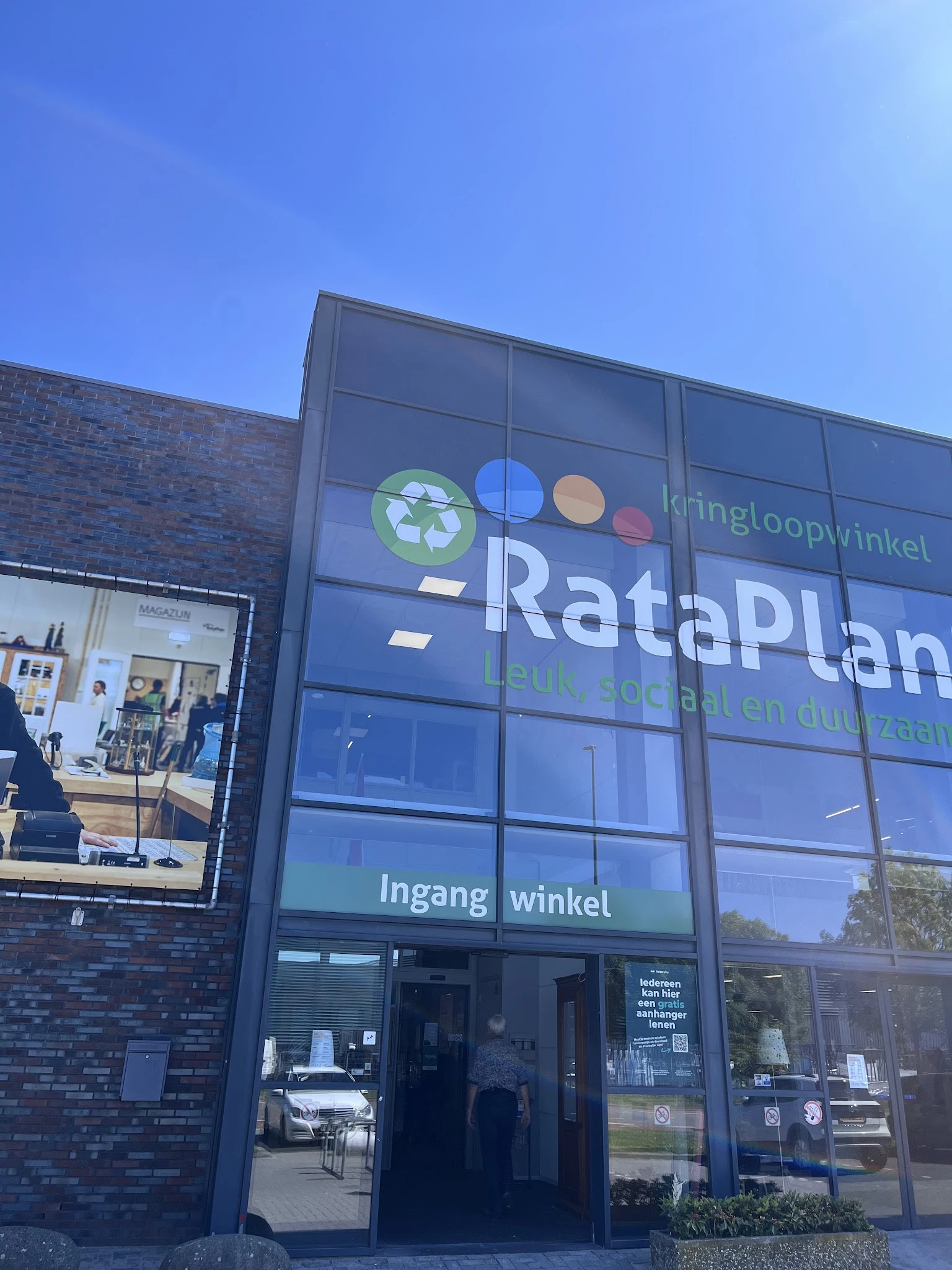 Glazen gevel van kringloopwinkel RataPlan met uithangbord en winkelramen