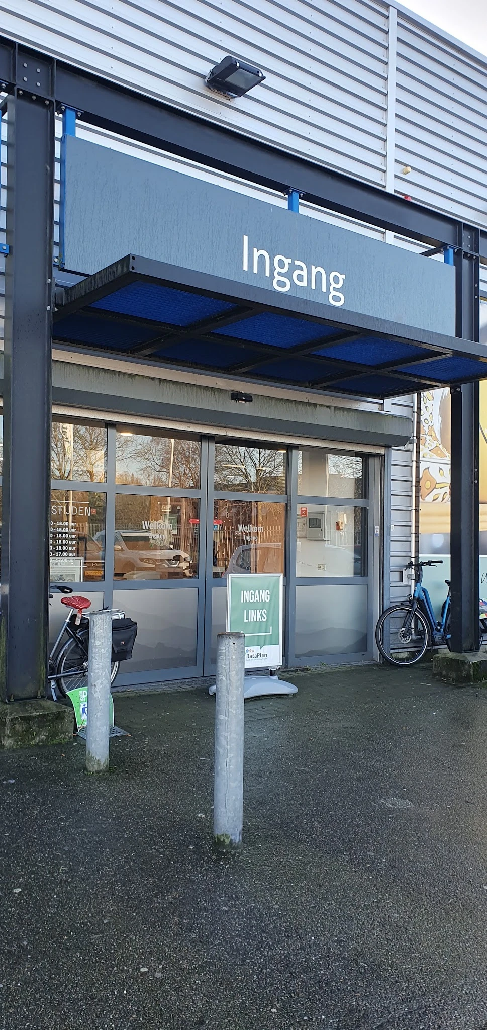 Winkelgevel met glazen deuren en ramen, ingangsbord 'INGANG LINKS', fietsen buiten