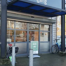 Winkelgevel met glazen deuren en ramen, ingangsbord 'INGANG LINKS', fietsen buiten