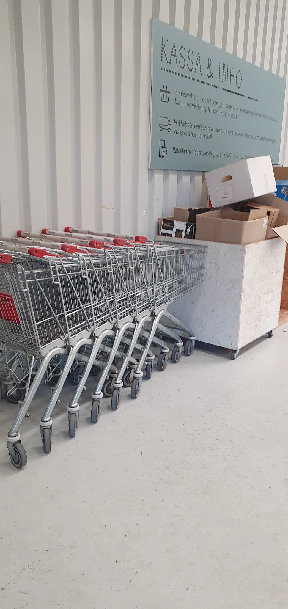 Winkelwagentjes met rode handgrepen opgesteld in een rij tegen de wand van de winkel