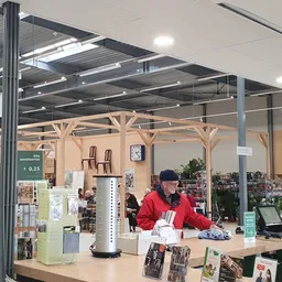 Binnenaanzicht van kringloopwinkel met glazen wand, houten kozijnen, medewerker achter toonbank en diverse artikelen op displ
