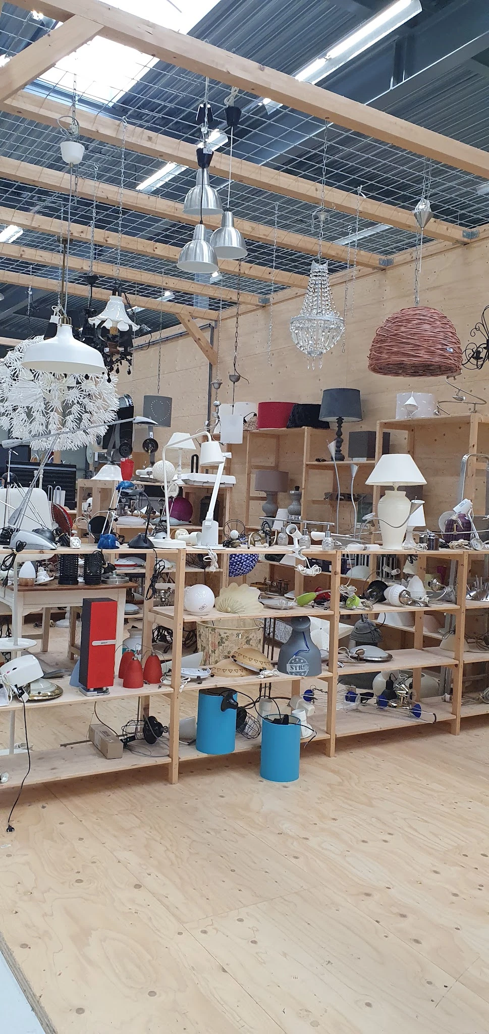 Houten stellingen vol huishoudelijke artikelen, lampen, servies en decoratieve items in een kringloopwinkel