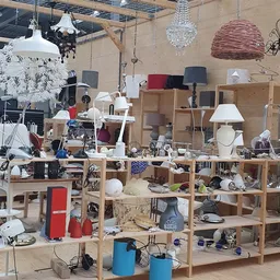 Houten stellingen vol huishoudelijke artikelen, lampen, servies en decoratieve items in een kringloopwinkel