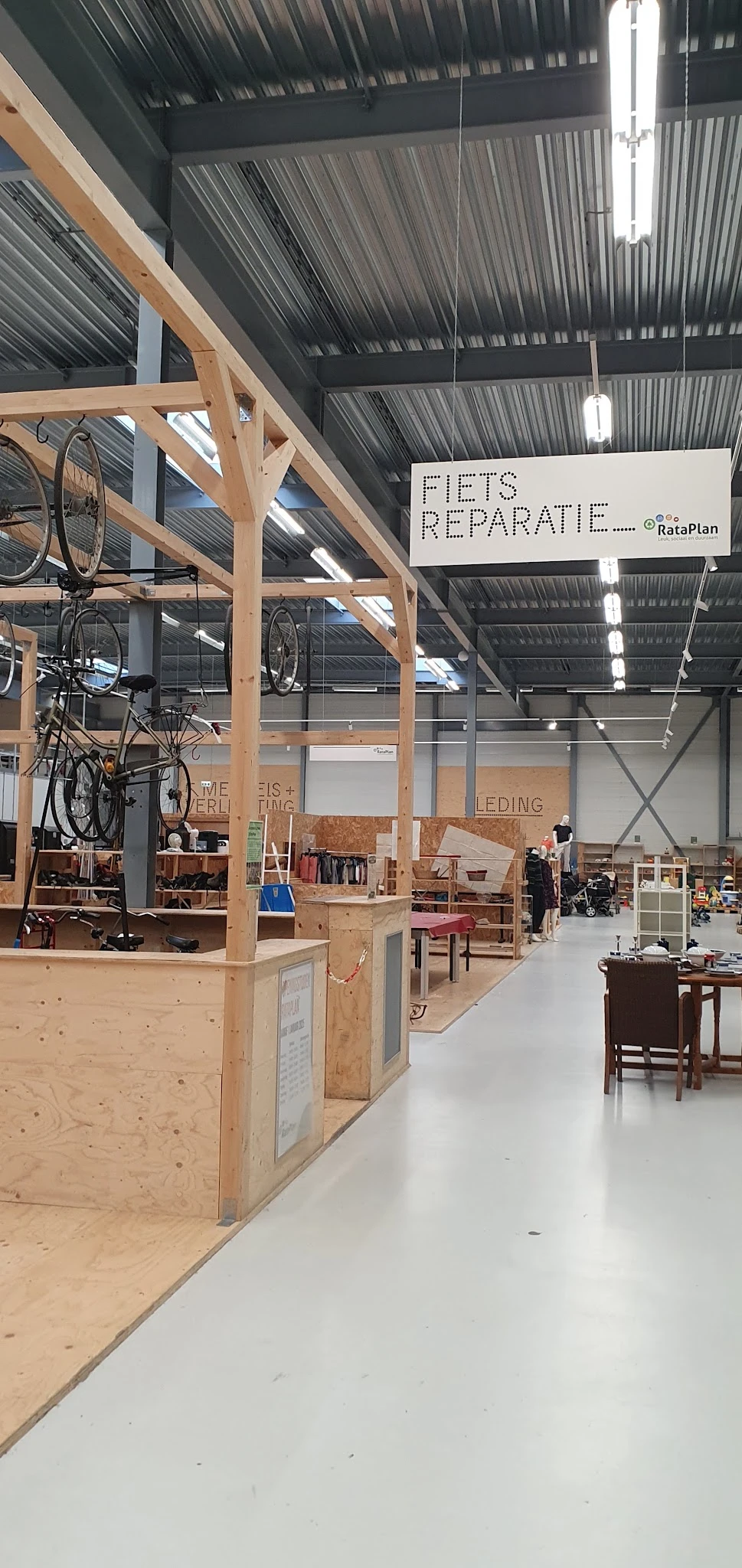 Ruim magazijnachtig interieur van kringloopwinkel met houten stellingen, meubels, fietsen en diversen items uitgestald