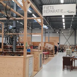 Ruim magazijnachtig interieur van kringloopwinkel met houten stellingen, meubels, fietsen en diversen items uitgestald