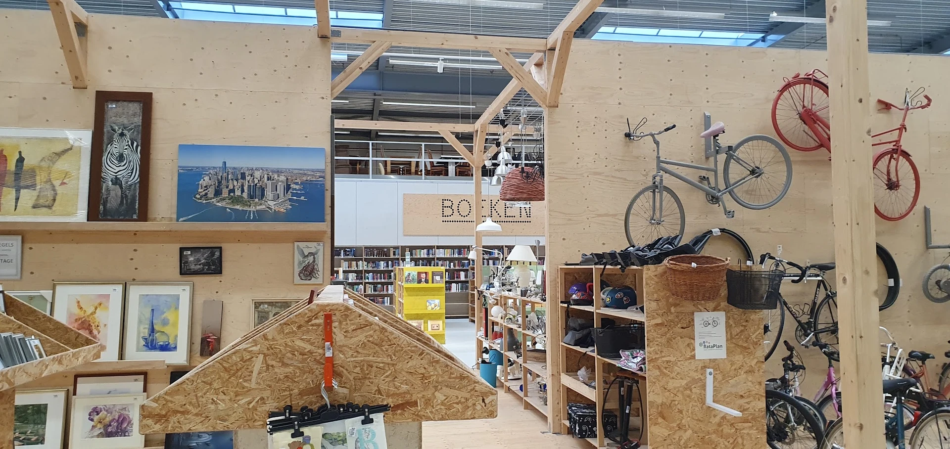 Ruim winkelinterieur met houten constructie, boekenkasten, een fiets aan de wand en diverse tweedehands spullen op planken