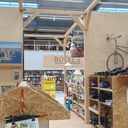 Ruim winkelinterieur met houten constructie, boekenkasten, een fiets aan de wand en diverse tweedehands spullen op planken