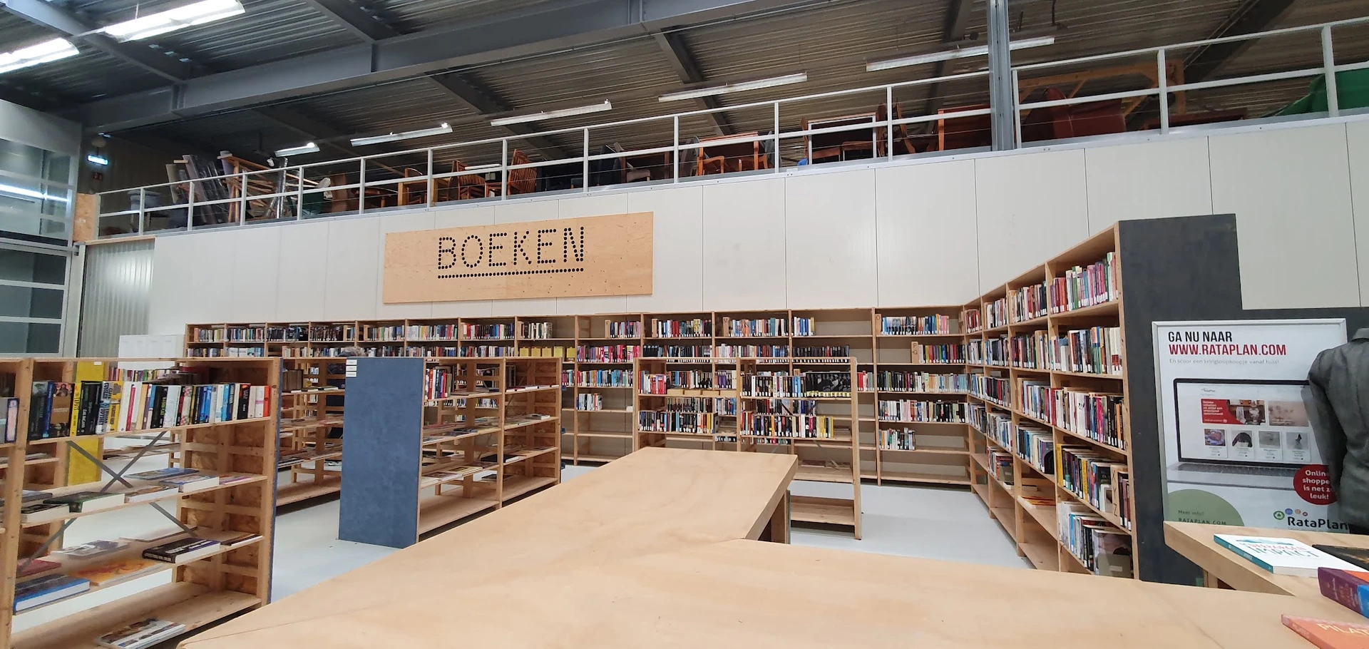 Boekengedeelte met houten stellingen vol boeken en een groot BOEKEN-bord aan de muur