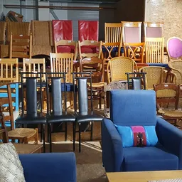 Diverse tweedehands meubels en stoelen uitgestald in de winkel, waaronder blauwe fauteuils, houten stoelen en een bankje