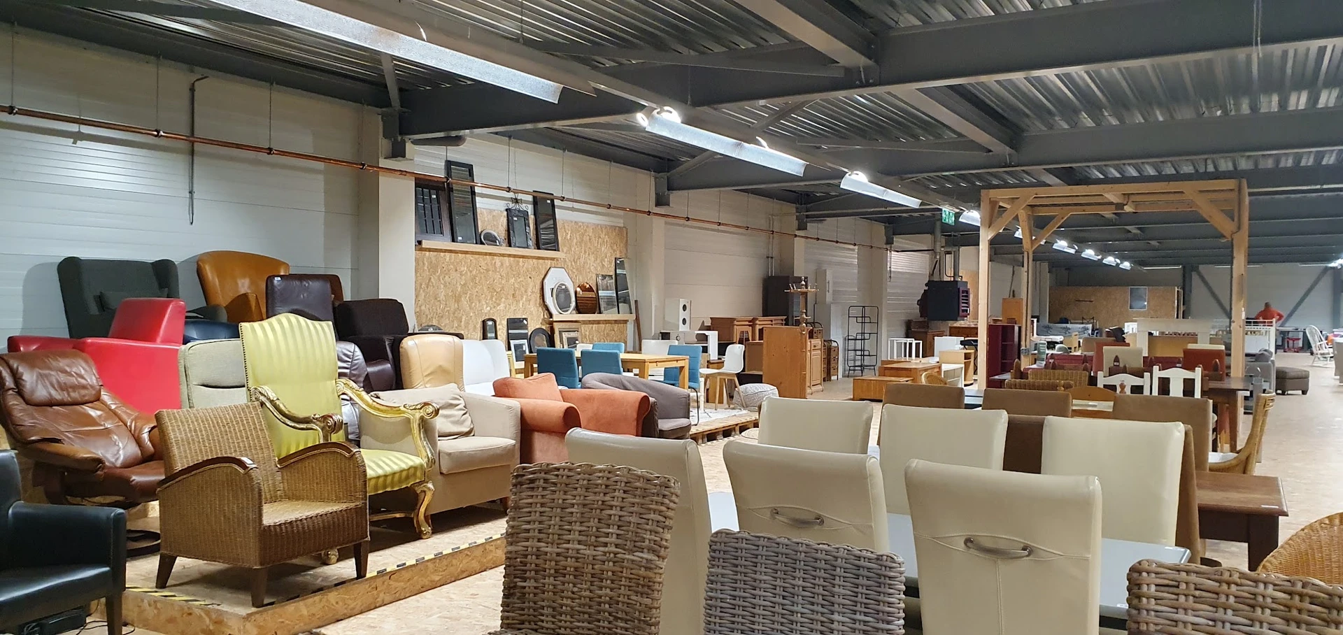 Winkelvloer met diverse meubels: stoelen, tafels, kasten en andere huisraad uitgestald in een groot pand